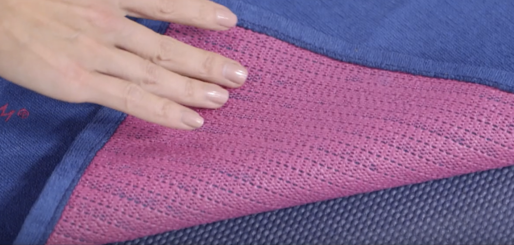 Hand displaying the back of a pink yoga towel with a blue top.