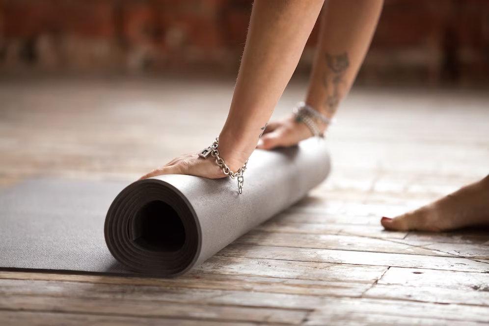 A gray yoga mat being rolled up and stored on a wooden floor
