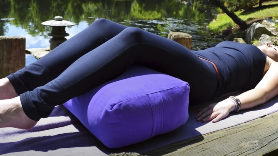 Image of a woman reclining with a blue rectangular bolster supporting her legs