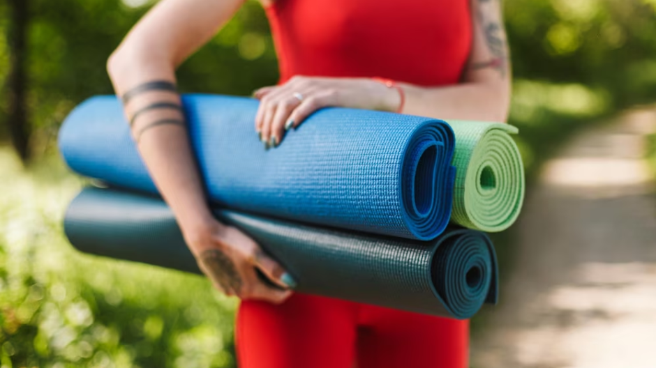 Image of a woman wearing red holding three yoga mats in various colors