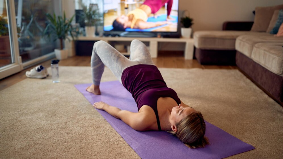 Image of a woman on a yoga mat mimicking yoga poses demonstrated on a television