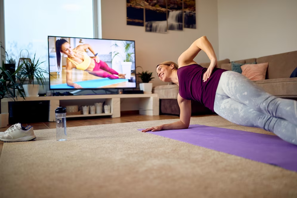 Image of a woman on a yoga mat mimicking yoga poses demonstrated on a television