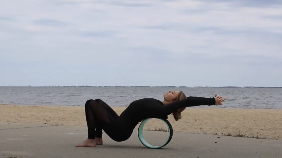 Image of a woman by the seashore using a yoga wheel to stretch her back