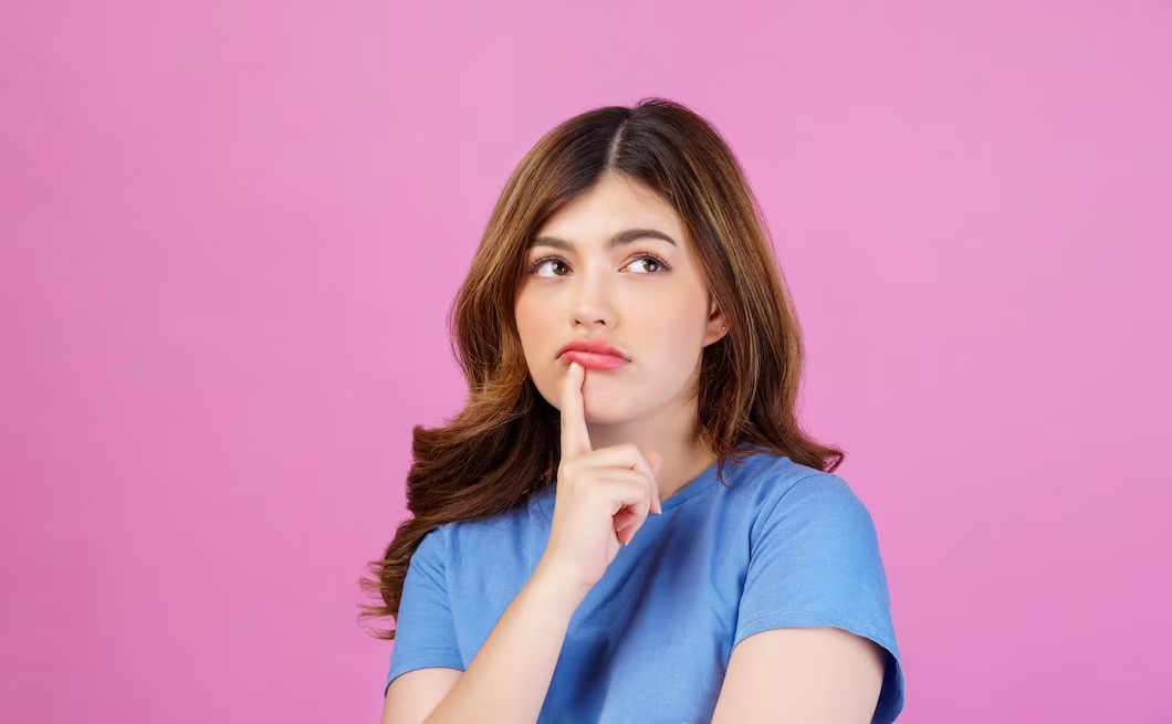 Image of a girl wearing a blue shirt, with her finger on her lips, looking upwards