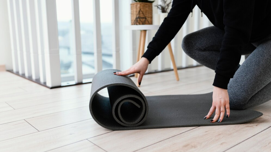 Image of someone unrolling a black yoga mat on a wooden floor