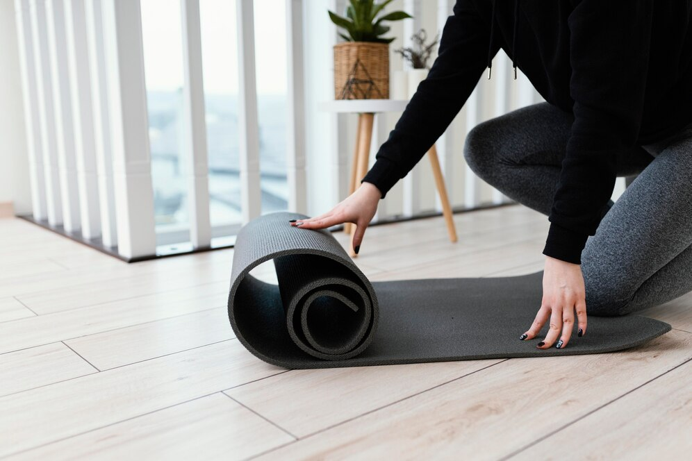 Image of someone unrolling a black yoga mat on a wooden floor