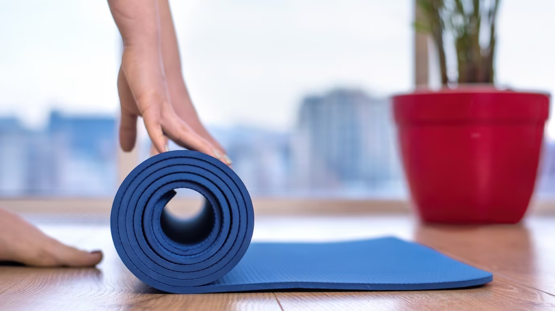 Image of someone rolling up a blue yoga mat on a wooden floor