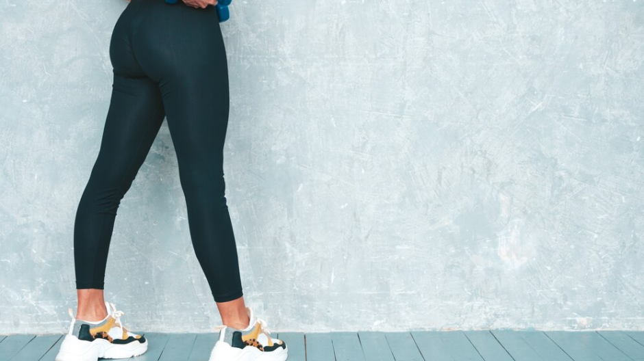 Back view of a female wearing black yoga pants, holding blue dumbbells.