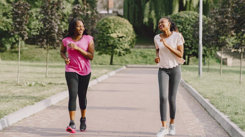Two females laughing and looking at each other while jogging in the park
