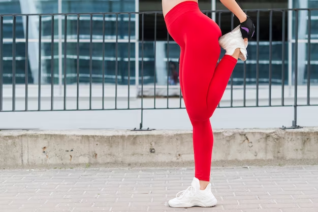 Image of a girl wearing red yoga pants stretching her lower body, holding her foot at the back